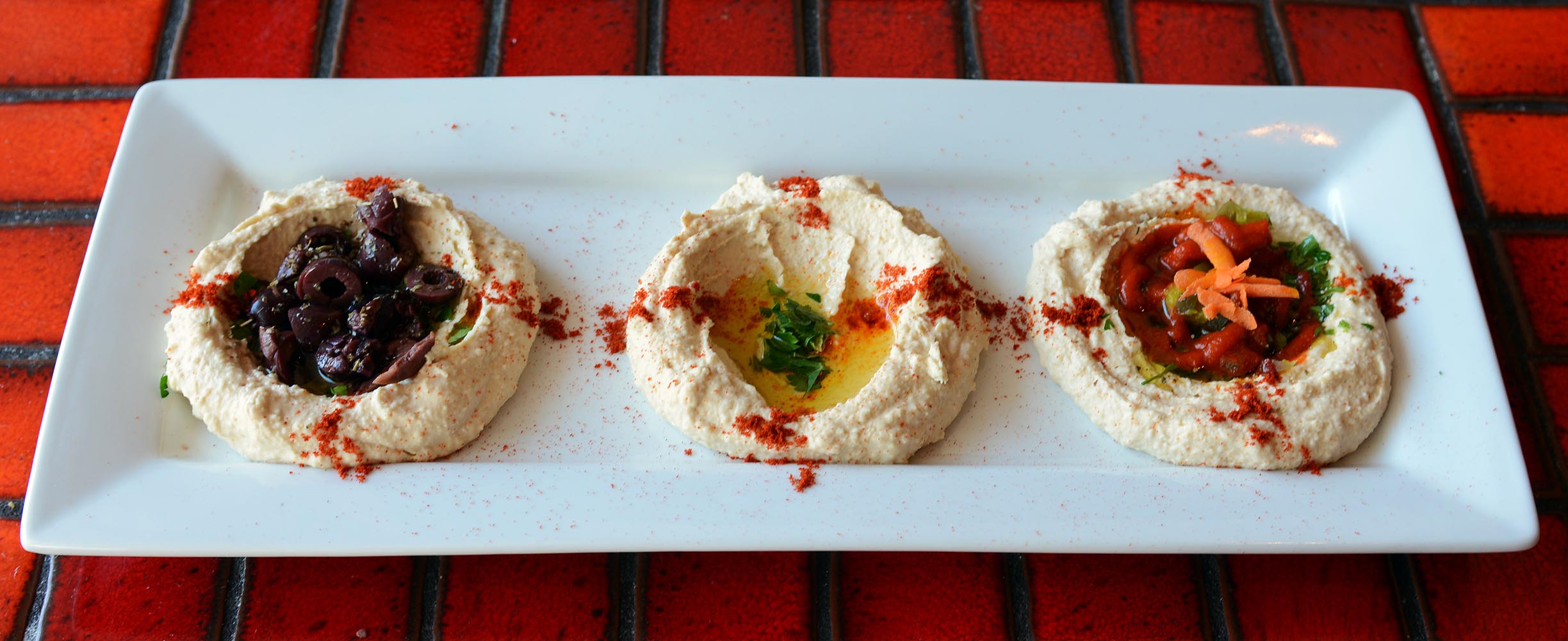 One of our restaurant's prefered appetizers: Hummus Trio, including our traditional hummus, kalamata olives hummus, and sriracha jalapeños hummus.